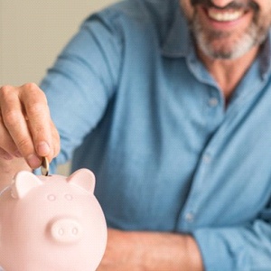 man putting coins into a pink piggy bank