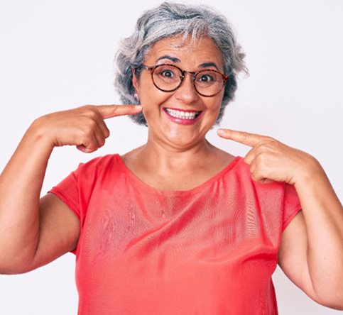Happy, mature woman pointing at her implant dentures