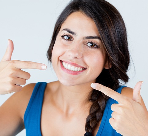 Woman pointing to her smile after porcelain veneer treatment